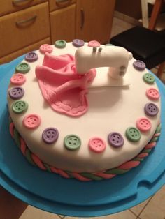 a cake decorated with buttons and a sewing machine on a blue plate in the kitchen