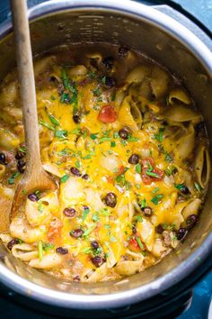 a pot filled with pasta and vegetables next to a wooden spoon