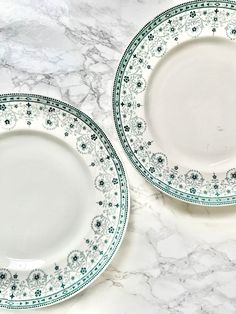 two white and green plates sitting on top of a marble countertop next to each other