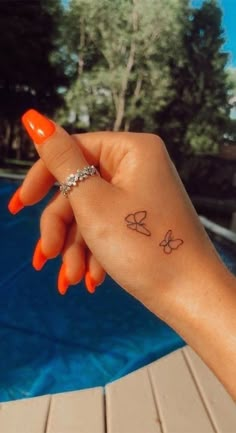 a woman's hand with a small butterfly tattoo on her left wrist next to a swimming pool