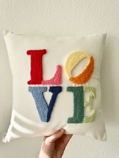 someone is holding up a pillow with the word love spelled in multicolored letters