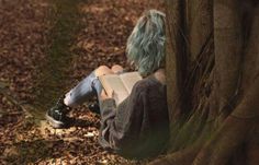 a person sitting on the ground next to a tree with a book in their lap