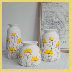 three white vases with yellow flowers painted on them next to a framed photo and map