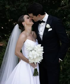 a bride and groom kissing in front of trees