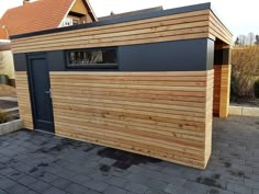 a small wooden building sitting on top of a brick road next to a house with a garage