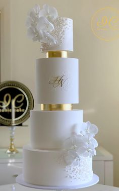 a three tiered wedding cake with white flowers and gold trimmings on top