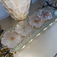 three glass flowers sitting on top of a metal tray next to a vase and lamp