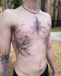 a shirtless man with tattoos on his chest standing in front of a tree and building