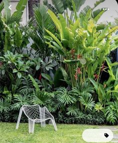 a white chair sitting in the middle of a lush green yard next to trees and bushes