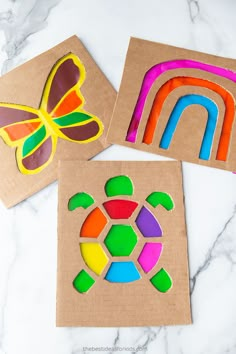 three different colored paper cut outs on top of a marble counter with a butterfly, turtle and rainbow in the middle