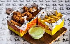 two boxes filled with chicken and french fries on top of a wooden tray next to dipping sauce