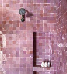 a bathroom with pink tiles on the shower wall and shelf for jars in the corner