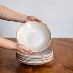 a stack of white plates being held by someone's hands on a wooden table