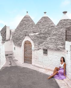 a woman sitting on the ground in front of an old building with stone roof tops