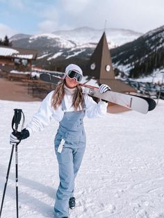 a woman in overalls and goggles holding a snowboard on top of her head