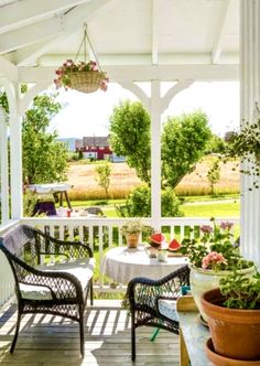 a porch with chairs, table and potted plants on the front porch area that overlooks an open field