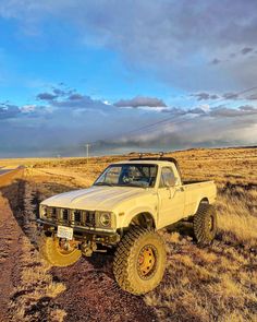 an off - road truck parked on the side of a dirt road near a field