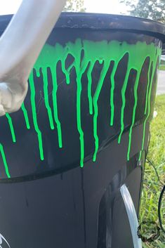 someone is painting the side of a black trash can with green drips on it