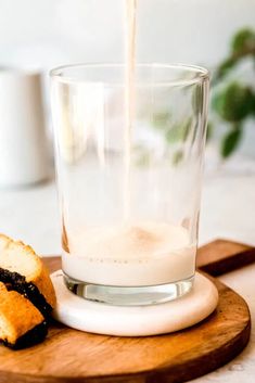 a glass of milk being poured into a cup on top of a cutting board next to bread