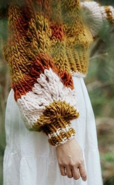 a woman wearing a knitted sweater and white dress with her hands in the air