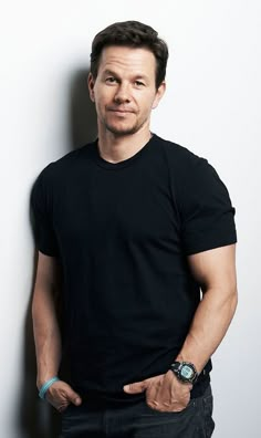 a man standing in front of a white wall wearing a black shirt and blue bracelet