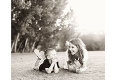 a woman laying on the ground next to a baby in black and white with trees behind her