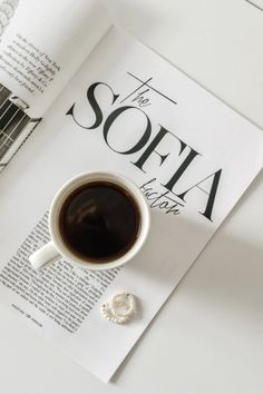 a cup of coffee sitting on top of a white table next to an open book