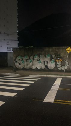 an empty street at night with graffiti on the wall and traffic lights in the background