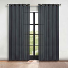 an open window with black curtains in front of a white wall and wooden flooring