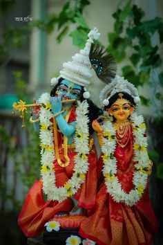 two statues of hindu deities in red and white outfits, one holding a flute while the other holds a bird