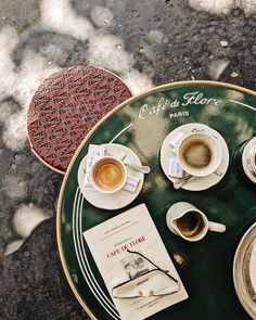 a table topped with coffee cups and saucers next to a book on top of a green plate