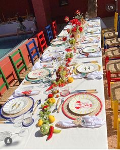 a long table is set with colorful plates and place settings for an outdoor dinner party