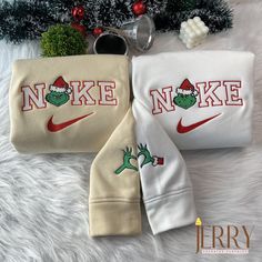 two sweatshirts with the words nike and grin face on them, sitting next to a christmas tree