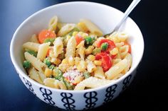 a bowl filled with pasta and vegetables on top of a blue tablecloth next to a fork