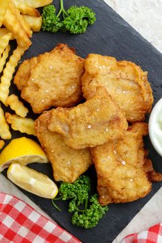 fried fish and french fries on a black slate platter next to lemon wedges