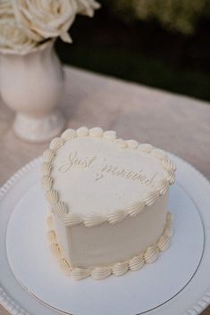 a heart shaped cake sitting on top of a white plate next to a vase with flowers