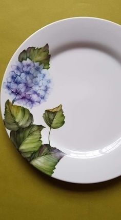 a white plate with blue and green flowers painted on the side, sitting on a yellow surface