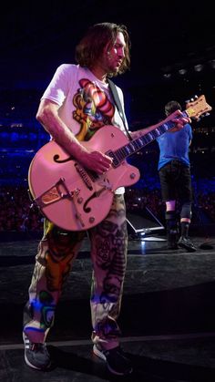 a man holding a pink guitar while standing on top of a stage