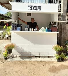 a man standing behind a white counter in front of a building with the words the coffee on it