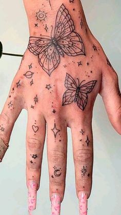 a woman's hand with tattoos on it and pink fingernails, holding a butterfly