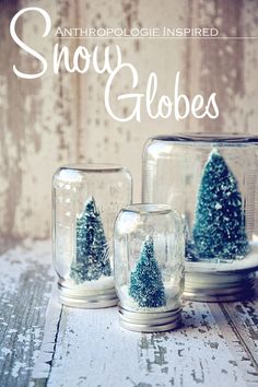 three glass jars with trees in them sitting on a table next to another jar filled with snow