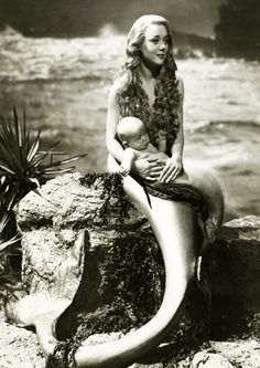 a woman holding a baby sitting on top of a rock next to the ocean,