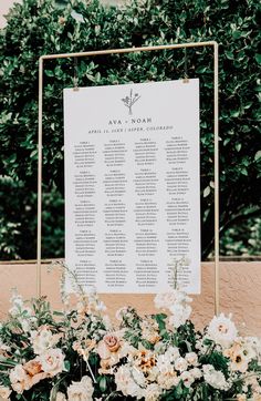 a seating chart with flowers and greenery in front of a sign for an outdoor ceremony