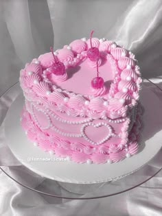 a pink heart shaped cake with cherries on top is sitting on a glass plate