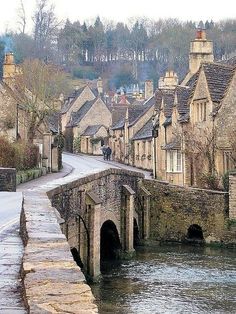 an old stone bridge over a river in the middle of a village with houses on either side