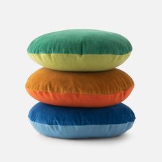 three pillows stacked on top of each other in different colors and sizes, one is blue, the other is orange