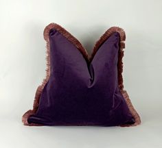 a purple and brown pillow with fringes on the bottom, sitting against a white wall