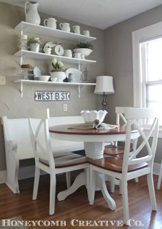 a dining room table with white chairs and plates on the wall above it, along with shelves filled with dishes