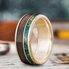 two wedding bands with green and yellow wood inlays on each band, sitting on top of a piece of paper