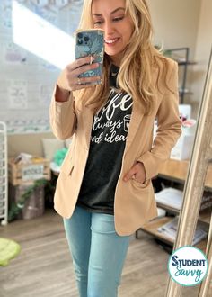 a woman taking a selfie in front of a mirror wearing jeans and a blazer